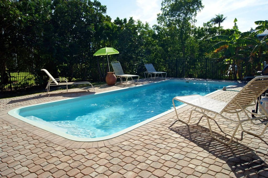 Rectangular pool with a paver deck and lounge chairs inside a black metal fence